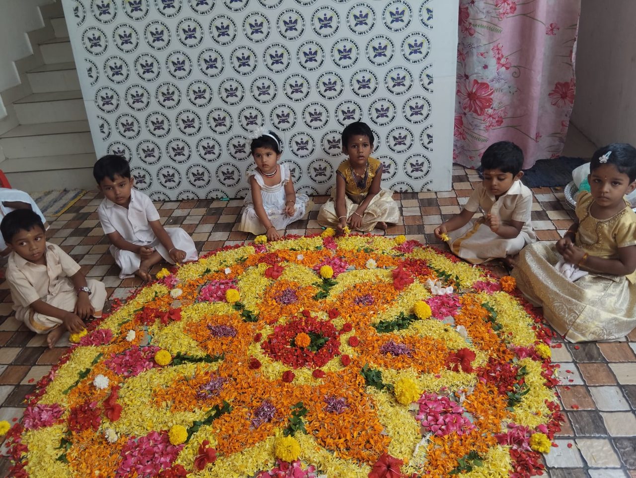Children sitting around a colourful flower pookalam during a festival celebration